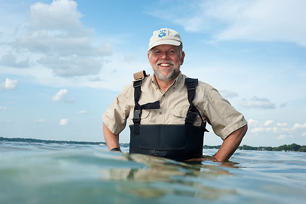 A person stands waist-deep in water in waders smiling