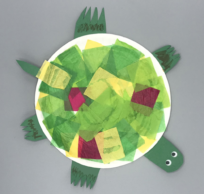 A paper plate craft of a turtle with crepe paper shell and green head, tail, and feet.
